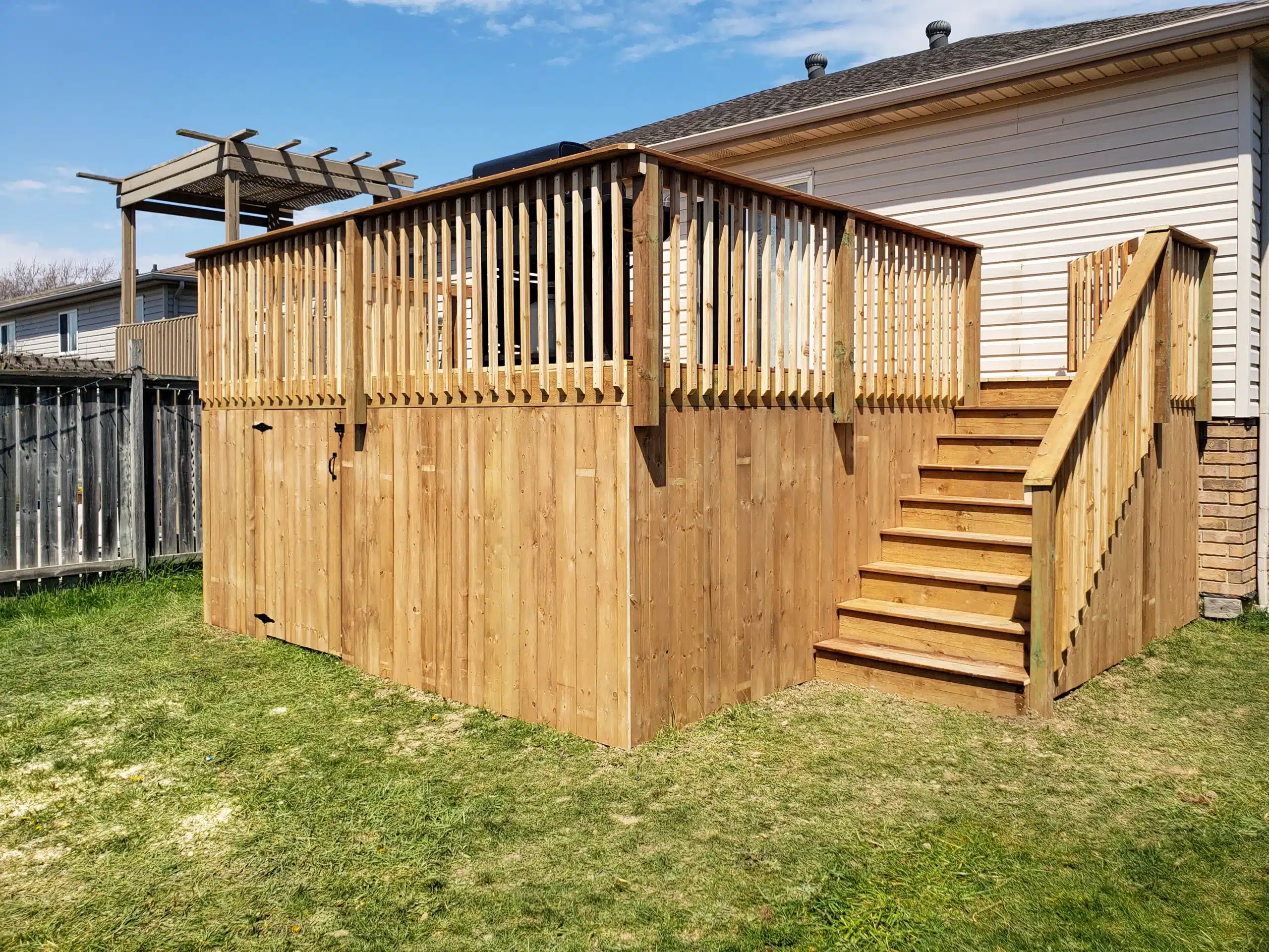 Elevated wooden deck with railing and staircase, attached to the back of a house with vinyl siding, set in a grassy backyard.